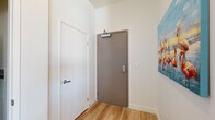 This contemporary single-floor residence showcases a thoughtfully designed open-concept layout with clean lines and modern finishes throughout. The entryway, finished with light wood-look flooring and crisp white walls, sets the tone for the space and is accented by a vibrant flamingo-themed artwork.

The living and dining area serves as the heart of the home, anchored by dramatic floor-to-ceiling windows that frame sweeping cityscape views and flood the space with abundant natural light. Light wood flooring flows seamlessly through this area, complementing the neutral tones of the interior. The dining nook features a glass-top round table, while the living area provides a comfortable and stylish setting with direct access to a balcony.

The kitchen is outfitted with warm wood cabinetry extending to the ceiling, stainless steel appliances including a gas range, over-the-range microwave, and a full-size refrigerator, all set against a light tile backsplash and matching wood-look floors.

The primary bedroom is generously sized with soft carpeted flooring and connects directly to an en-suite bathroom featuring a dual-sink vanity with wood cabinetry, a white quartz countertop, large-format tile flooring, and tall ceilings that lend an airy feel. A second bedroom enjoys its own large window with expansive city views. The second bathroom includes a soaking tub with marble-style tile surround, a single-sink vanity, and slate tile flooring.