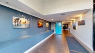Located at 1227 Federal Ave in the West Los Angeles neighborhood of Los Angeles, CA, this building lobby offers a well-designed and welcoming arrival experience. The space features notably high ceilings with crown molding, creating an open and airy atmosphere that feels larger than its footprint suggests. The walls are finished in a contemporary two-tone scheme — a deep blue-gray on the lower half and crisp white above — lending the space a modern, polished character.

A series of vibrant Los Angeles-themed photographic art pieces lines the walls, celebrating iconic local imagery such as Venice Beach palm trees, surfers, and city street scenes, reinforcing the building's strong sense of place. A built-in bench runs along one wall, providing a practical seating area for residents and guests. Durable tile flooring extends throughout, complemented by carpet runners near the entrance for easy maintenance.

A standout feature is the Amazon Hub package locker station in a bold turquoise finish, offering residents convenient and secure parcel retrieval. The entrance vestibule is framed by floor-to-ceiling glass walls and sliding doors, flooding the lobby with natural light and providing views of a landscaped courtyard with a circular planter feature. Recessed and wall-mounted lighting ensure the space is well-lit at all hours, completing a functional yet stylish lobby environment.