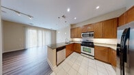 Located at 2323 Dulles Station Blvd in Herndon, Virginia, this well-appointed single-floor residence offers a thoughtfully designed layout with modern finishes throughout. The kitchen serves as a central highlight, featuring warm medium-toned wood cabinetry, granite countertops, a large center island with a built-in sink, stainless steel appliances including a gas range, microwave, refrigerator, and dishwasher, along with elegant pendant lighting and tile flooring. The open layout connects seamlessly to the living area, which is bathed in natural light through floor-to-ceiling sliding glass doors dressed with vertical blinds, opening to an outdoor space. Wood-style flooring extends through the main living areas, creating a cohesive and polished aesthetic. The bedroom is generously sized, with plush carpet, a ceiling fan, and a bright window offering natural views. The bathroom is finished with crisp white cabinetry, a dark granite vanity top, and wood-style flooring, lending a clean and contemporary feel. A dedicated in-unit laundry room with a full-size washer and dryer adds everyday convenience. Neutral wall tones and recessed lighting throughout contribute to a bright, welcoming ambiance suited for comfortable modern living.