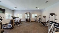 Located at 26 N Ladow Ave in Millville, NJ, this fitness center offers a well-equipped, single-floor space designed to accommodate a full range of workout routines. The room features neutral gray walls, recessed lighting, and durable patterned carpet tiles throughout, creating a clean and functional environment.

The cardio section is generously appointed with multiple treadmills, elliptical trainers, and stationary bikes, complemented by wall-mounted flat-screen televisions to keep users engaged during their workouts. Natural light filters in through several windows fitted with white blinds, enhancing the overall brightness of the space.

The strength-training area includes a variety of cable machines, selectorized weight machines for targeted muscle groups, adjustable benches, and a multi-functional cable crossover tower, providing options for both isolated and compound exercises. Equipment is organized to allow comfortable circulation throughout the room.

Additional amenities include wall-mounted accessory storage, a sanitizing station near the entrance, and informational postings. Double doors provide easy access to and from the facility. The layout is thoughtfully arranged to maximize usable floor space while maintaining an open, uncluttered feel, making this fitness center a practical and accessible resource for residents.