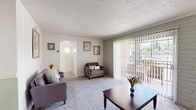 Located at 6300 Montgomery Blvd NE in Albuquerque, New Mexico, this one-bedroom, two-bathroom residence offers a well-organized single-floor layout designed for comfortable everyday living. The living room features plush carpeting, a painted brick accent wall, and large sliding glass doors dressed with vertical blinds that invite natural light and provide direct access to an outdoor area. The adjoining dining room continues the warm, functional aesthetic with a ceiling fan overhead, wainscoting along the lower walls, and a sliding glass door that frames views of lush greenery outside. The galley-style kitchen is efficiently arranged with white cabinetry, black hardware, light countertops, wood-look flooring, and white appliances including a refrigerator and electric range. The generously sized bedroom showcases another striking painted brick accent wall, soft carpeting, a large sliding closet, and a window that allows natural light to filter in. Two bathrooms serve the unit, each clean and bright — one featuring a vanity with ample counter space and white cabinetry leading to a tub-shower combination, and the second offering a compact tub-shower setup with wood-look flooring. A dedicated closet provides additional storage to complete this practical and inviting home.