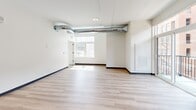 Located at 2930 Smallman St in Pittsburgh's vibrant Strip District, this one-bedroom, one-bathroom unit offers a thoughtfully designed layout with a clean, modern aesthetic. The open-concept living and kitchen area is anchored by light wood-tone flooring that runs throughout, bright white walls, and a distinctive industrial character courtesy of exposed metallic ductwork running across the ceiling — a bold architectural detail that adds visual interest to the space.

The kitchen is well-appointed with light wood cabinetry, white subway tile backsplash, white quartz-style countertops, and a full suite of stainless steel appliances including a range, microwave, dishwasher, and refrigerator. A window beside the kitchen frames views of the surrounding urban streetscape, flooding the area with natural light.

The living area is generously open, with additional windows that bring in ample daylight and views of the neighboring architecture. The bedroom features plush carpeting, two windows that offer good natural light, a closet, and continued exposure to the space's industrial design language. The full bathroom is finished with light wood vanity cabinetry, a tub/shower combo, and light wood-tone flooring, maintaining the unit's cohesive modern palette throughout.