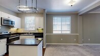 Located at 5050 Hacienda Dr in Dublin, CA, this single-floor residence offers a well-designed layout with a cohesive, neutral color palette and thoughtful finishes throughout. The kitchen is a standout feature, equipped with stainless steel appliances including a refrigerator, range, microwave, and dishwasher. White shaker cabinetry pairs with dark granite countertops and rich hardwood flooring, while a central island provides additional workspace and storage. A distinctive hanging pot rack adds a functional, chef-inspired touch overhead. The kitchen opens seamlessly into the dining and living areas, which are finished with plush wall-to-wall carpeting and crown molding. Multiple windows fitted with white horizontal blinds fill these spaces with natural light and offer views of the surrounding greenery. A ceiling fan in the living area enhances comfort. The bedroom features built-in shelving along one wall, a ceiling fan, a window with natural light, and soft carpeting. The bathroom is clean and functional, offering a full tub-shower combo with white tile surround and white cabinetry for storage. A fireplace is also visible in the floor plan, adding a warm focal point to the living area. Crown molding and consistent neutral-toned walls tie the entire home together with a polished, uniform aesthetic.