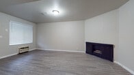 This single-floor residence offers a thoughtfully laid-out interior with a clean, neutral aesthetic throughout. The spacious living room serves as the heart of the home, showcasing light gray laminate wood flooring, soft neutral walls, white baseboards, and a classic dark-framed fireplace that adds a focal point to the room. A window provides natural light, completing the open and airy feel of the space.

The galley-style kitchen is efficiently designed with white cabinetry lining both sides, bold dark granite countertops, a stainless steel sink, and a full suite of appliances including a refrigerator, range, and dishwasher. A window at the end of the kitchen brings in additional natural light, enhancing the functional workspace.

The bedroom features plush wall-to-wall carpeting, a ceiling fan with light fixture, and a large closet with vertical blinds, offering ample storage. Exposed beam detailing adds architectural character to the room.

An additional room with laminate flooring connects to a hallway, providing flexible space for various uses. The bathroom is appointed with a white vanity, dark granite countertop with an oval undermount sink, a large mirror, and a tiled shower and tub combination. Consistent finishes across the kitchen and bathroom tie the home together cohesively.