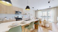 Located at 3001 W Belmont Ave in Chicago's vibrant Belmont-Cragin neighborhood, this thoughtfully designed 2-bedroom, 2-bathroom residence offers a bright, modern aesthetic across a well-utilized single floor. Light oak hardwood flooring runs throughout, tying the open-concept living spaces together seamlessly.

The kitchen is a standout feature, showcasing light wood cabinetry, a white subway tile backsplash, stainless steel appliances, and a generous island with a waterfall-edge countertop and bar seating for three — all anchored by striking black pendant lights with gold interiors. The kitchen flows directly into the living room, which is bathed in natural light from floor-to-ceiling sliding glass doors that open to a private balcony with neighborhood views. A built-in electric fireplace adds a refined focal point to the living area.

Both bedrooms are serene and well-lit, with large windows dressed in sheer curtains. The spacious primary bedroom comfortably accommodates a full suite of furnishings. The two bathrooms are finished with modern large-format tile, a wall-mounted toilet, and a tub-shower combination with decorative tile surround and black-framed glass enclosure, reflecting a clean, contemporary design sensibility throughout.
