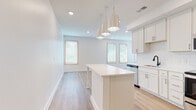 Located at 1115 Seigle Ave in Charlotte, NC, this single-story unit offers a clean, modern aesthetic defined by a bright, neutral palette and light hardwood-style flooring that flows consistently throughout the space. The open-concept kitchen serves as a central highlight, featuring white shaker cabinetry, white quartz countertops, a classic subway tile backsplash, and a full suite of stainless steel appliances including a French door refrigerator, electric range, built-in microwave, and dishwasher. A central kitchen island with pendant lighting above provides additional workspace and casual seating, while multiple windows invite generous natural light into the adjoining living and dining areas. The living space is generously proportioned, with recessed lighting and large windows fitted with wood-framed blinds that frame views of surrounding greenery. The bedrooms are well-sized, each featuring light hardwood-style flooring, natural light from wood-trimmed windows, and clean white walls. The bathrooms are finished with white cabinetry, dark quartz countertops, and light tile flooring. One full bathroom includes a tiled tub-shower combination with matte black fixtures, while an additional bathroom provides a single vanity with ample storage. Overall, the unit presents a cohesive, move-in-ready interior with contemporary finishes throughout.