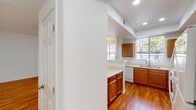 This single-story residence offers a thoughtfully designed layout that balances practicality and comfort. The kitchen is a standout feature, showcasing warm honey-toned wood cabinetry, light countertops, and hardwood flooring. Recessed lighting and a tray ceiling add architectural interest overhead, while large windows invite generous natural light and outdoor views. A peninsula-style counter creates a natural division between the kitchen and the adjoining living areas, enhancing the open flow of the floor plan. White appliances, including a range, microwave, dishwasher, and refrigerator, are seamlessly integrated into the cabinetry. A dedicated in-unit laundry room with side-by-side washer and dryer hookups adds everyday convenience. The carpeted hallway leads to the bedrooms and bathroom, providing a soft transition from the hard-surface living areas. The bathroom features warm wood vanity cabinetry, light tile flooring, and a full tub-shower combination with white tile surround and chrome fixtures. Bedrooms are finished with neutral carpet and vertical blinds covering sliding glass doors that allow for additional natural light. Ceiling fans are present in multiple rooms, enhancing comfort throughout. The overall aesthetic is clean, cohesive, and move-in ready.