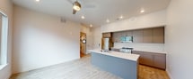 Located at 455 W 500 S in Salt Lake City, UT, this modern 570-square-foot, one-bedroom, one-bathroom apartment is designed with clean lines and contemporary finishes. Light hardwood-style flooring runs throughout the entire unit, creating a cohesive and bright aesthetic. The open-concept kitchen and living area serves as the heart of the home, featuring a large central island with a white quartz countertop, an undermount sink, and a gray base. The kitchen is equipped with stainless steel appliances, including a gas range, microwave, and refrigerator, complemented by two-toned upper and lower cabinetry in brown and gray. Recessed lighting and a ceiling fan provide both illumination and comfort in the living area, which receives natural light through a large window. A barn-style door leads to an in-unit laundry area. The 160-square-foot bedroom is a serene, light-filled space with a large window and clean white walls. The full bathroom features a tiled shower-tub combination with a curved curtain rod, brushed nickel hardware, and a recessed light. A hallway connects all rooms efficiently, completing this well-appointed urban apartment.