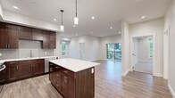 This well-appointed single-floor residence showcases a thoughtfully designed open-concept layout that seamlessly connects the kitchen and living areas. The kitchen is a standout feature, equipped with rich dark-wood cabinetry, stainless steel appliances including a range, microwave, and dishwasher, a gray subway tile backsplash, and crisp white countertops. A central island with pendant lighting provides additional prep space and a natural gathering point. Durable wood-look flooring runs throughout the main living areas, complementing the neutral, light-toned walls and recessed lighting overhead. The living area opens to a private balcony through sliding glass doors, offering pleasant views of surrounding greenery and the neighboring streetscape. The bedrooms are carpeted for comfort, with large windows that bring in abundant natural light and outdoor views. A walk-in closet adds practical storage to the bedroom wing. The primary bathroom features a frameless glass walk-in shower, double-sink vanity with dark wood cabinetry, and wood-look flooring, while a second bathroom offers a full soaking tub. A dedicated utility area houses the water heater, and in-unit laundry connections are also present, rounding out this functional and modern living space.