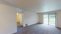 Located at 4302 Alpenhorn Dr NW in Comstock Park, Michigan, this single-floor residence offers a thoughtfully laid-out interior with a variety of functional spaces. The standout architectural feature is a curved living area enclosed by a sweeping bank of five windows, flooding the room with natural light and providing an open, airy feel. The main living room is generously proportioned with plush carpet flooring and a sliding glass door fitted with vertical blinds that opens to an outdoor patio, offering views of surrounding greenery. The layout connects seamlessly to a hallway leading to the private quarters of the home. The bedroom features soft carpet flooring, a ceiling fan with integrated lighting, and a louvered closet door providing ample storage. The kitchen is equipped with rich wood-toned cabinetry offering substantial storage, a double-basin stainless steel sink, light-toned countertops, and a dishwasher. The bathroom includes a full tub-and-shower combination with built-in shelving, tile flooring, and a vanity with storage. Throughout the home, neutral wall tones and carpet create a clean, cohesive aesthetic, while consistent HVAC venting underscores the unit's practical design.