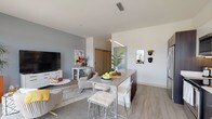 This single-floor residence showcases a contemporary open-concept layout that seamlessly connects the kitchen, dining, and living areas. The kitchen is well-appointed with stainless steel appliances, including a French door refrigerator, electric range, built-in microwave, and dishwasher. Sleek dark wood cabinetry contrasts with white upper cabinets and light-toned countertops, creating a modern aesthetic. Under-cabinet lighting and light wood-style flooring enhance the clean, functional design. A kitchen island with bar seating and a linear pendant light serves as a natural dividing point between the kitchen and the open dining area.

The living room benefits from large sliding glass doors that invite abundant natural light and provide access to a private balcony with outdoor views. A soothing gray accent wall anchors the living area, adding depth to the bright, airy space.

The bedroom features plush carpeting, a charcoal accent wall, and wall-mounted shelving, offering a cozy and practical retreat. The bathroom includes a spacious glass-enclosed walk-in shower, light wood-style tile flooring, a vanity with ample counter space, and built-in open shelving for storage. Throughout, the design maintains a cohesive modern palette of neutral tones and quality finishes.