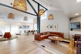 Located at 2052 Wilkins Ave in Napa, California, this thoughtfully designed single-floor community space offers an inviting and versatile gathering environment. The interior is anchored by dramatic vaulted ceilings supported by bold dark-painted structural beams, creating an airy, loft-like atmosphere throughout the open-plan layout. Light hardwood flooring flows seamlessly underfoot, complementing the bright white walls and curated colorful artwork displayed throughout.

The living area is centered around a rich cognac leather sectional sofa paired with a live-edge wood coffee table, all set atop a layered area rug. A stone-accented feature wall frames a wall-mounted flat-screen television, flanked by additional seating for relaxed gatherings. Woven rattan pendant lights hang at varying heights, adding warmth and an artisanal touch to the space.

The dining area accommodates a generous wooden dining table surrounded by an eclectic mix of modern chairs, ideal for communal meals or meetings. Large roller shades provide privacy while maintaining a clean, minimal aesthetic.

A standout bar counter with warm wood paneling and sleek bar stools sits beneath soaring teal-painted walls, with French doors opening directly to the outdoor pool area, seamlessly connecting indoor and outdoor living. The grounds feature manicured landscaping, a gated entrance, and a sparkling community pool with lounge seating.