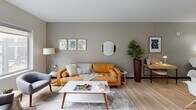 This single-floor residence showcases a thoughtfully designed open-concept layout that seamlessly connects the kitchen, dining, and living areas. Light hardwood flooring extends throughout the main living spaces, complementing the soft gray walls and creating a bright, airy atmosphere enhanced by generous natural light from large windows.

The kitchen is outfitted with rich dark cabinetry reaching to the ceiling, a full suite of stainless steel appliances including a refrigerator, range, microwave, and dishwasher, and a spacious dark-base island topped with a white countertop that provides ample bar seating. The open dining area accommodates both a round pedestal table with modern chairs and additional seating at the kitchen island.

The living room offers a comfortable, open atmosphere with large windows that invite natural light, creating a welcoming gathering space. Two bedrooms provide a private retreat; one features exposed industrial ductwork, a ceiling fan, and direct access to a bathroom, while the second includes a window overlooking a private balcony. Plush carpeting in the bedrooms adds warmth and comfort. The bathroom features light hardwood flooring, gray walls, and dark trim accents, maintaining the consistent modern aesthetic found throughout the residence.
