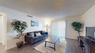 This single-floor residence offers a thoughtfully organized layout that balances functionality and comfort throughout its key living spaces. The living room serves as the central gathering area, featuring wood-style flooring, a textured ceiling, and a large sliding glass door flanked by vertical blinds that invite natural light and provide outdoor access. The open flow continues into the dining area, which connects seamlessly to the kitchen via a pass-through counter, making it ideal for everyday living and entertaining. The galley-style kitchen is equipped with black appliances including a refrigerator, electric range, microwave, and dishwasher, all complemented by white cabinetry and ample counter space. Two bedrooms provide comfortable retreats, each carpeted and featuring mirrored sliding closet doors that enhance the sense of space. Both rooms benefit from natural light through vertical-blind-covered windows, and the primary bedroom includes a ceiling fan. The bathroom features a single vanity with white cabinetry, a large mirror, and bright overhead lighting. Wood-style flooring runs throughout the main living areas, tying the space together with a clean, cohesive aesthetic.