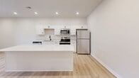 Located at 8484 Brougham Dr in Sterling Heights, MI, this one-bedroom, one-bathroom unit offers a thoughtfully designed single-floor layout with clean, modern finishes throughout. Light hardwood-style flooring runs continuously across every room, creating a cohesive and bright aesthetic.

The kitchen is a standout feature, showcasing white shaker cabinetry, light quartz countertops, a classic subway tile backsplash, and a full suite of stainless steel appliances including a refrigerator, gas range, built-in microwave, and dishwasher. A generous kitchen island provides additional prep and dining space, while recessed lighting illuminates the area efficiently.

The bedroom is a comfortable, well-proportioned space with neutral walls and a window fitted with blinds that allow for natural light and privacy. The clean, minimalist design makes it an adaptable and functional room.

The bathroom features a sleek walk-in shower enclosed by a sliding glass door with matte black framing, complemented by crisp white walls and consistent flooring. The dedicated laundry room includes a stacked washer and dryer unit along with open wire shelving for additional storage. The overall design palette—neutral tones, white trim, and black hardware accents—gives the space a modern, move-in-ready feel.