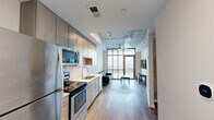 Located at 28 Woolfe St in Charleston, SC, this one-bedroom, one-bathroom unit offers a thoughtfully designed open-concept layout that maximizes its efficient footprint. The combined kitchen and living area forms the heart of the space, anchored by a galley-style kitchen outfitted with stainless steel appliances — including a refrigerator, electric range, microwave, and dishwasher — complemented by light wood-grain cabinetry, white quartz countertops, and a subtle tile backsplash. Wood-look flooring runs throughout the main living areas, adding warmth and continuity. The living room is distinguished by an exposed concrete ceiling with a ceiling fan, lending an industrial-modern character to the space. Floor-to-ceiling windows flood the room with natural light and open directly onto a private balcony, offering elevated views of the Charleston skyline. The bedroom provides a comfortable, private retreat, while the bathroom features clean white tile, a soaking tub with shower combo, and a wood-toned vanity. An in-unit laundry area adds everyday convenience. This well-appointed unit blends contemporary design with urban practicality in the heart of Charleston.