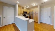 This single-floor unit offers a thoughtfully designed layout that balances open living spaces with functional private areas. The expansive living and dining area features a combination of hardwood-style flooring and plush carpeting, creating a warm and inviting atmosphere. A sliding glass door floods the space with natural light and provides views of the surrounding neighborhood. A pendant light adds a subtle decorative touch overhead.

The kitchen is efficiently designed with light wood cabinetry offering ample storage, stainless steel appliances including a refrigerator, electric range, and microwave, and a central island with a white countertop that provides additional workspace and casual seating. Recessed and flush-mount lighting keeps the area bright and functional.

The bedrooms are carpeted and finished with neutral beige tones, offering a comfortable and quiet retreat. Each room features windows that bring in natural light and outdoor views of mature trees and surrounding buildings. One bedroom includes a ceiling fan with a built-in light fixture.

Two bathrooms serve the unit, both featuring walk-in showers with sliding glass doors, light wood vanities with white countertops, and stone-look tile flooring. One bathroom includes a double vanity and towel bars, while the other offers a single vanity with a well-lit mirror and vanity lighting.