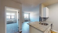 This single-floor residence offers a thoughtfully designed layout that balances comfort and functionality. The open-concept kitchen flows seamlessly into the living area, anchored by a granite-topped breakfast bar with an undermount sink — an ideal space for casual dining or entertaining. The kitchen is equipped with stainless steel appliances, including a full-size refrigerator and range, complemented by white cabinetry with modern hardware and warm wood-tone flooring that extends into the living space.

The living area is bright and welcoming, featuring hardwood-style flooring, neutral gray walls, and a large window with a wall-unit HVAC system beneath it, offering urban views of the surrounding cityscape. A second window in the adjacent room further enhances the natural light throughout.

The unit includes two bedrooms, each finished with plush carpeting, soft neutral tones, and bi-fold closet doors that open to roomy storage with built-in shelving. The full bathroom features a soaking tub and shower combination with classic white tile surround, chrome fixtures, and a granite vanity countertop. Clean lines and a neutral palette throughout create a cohesive, move-in-ready aesthetic.