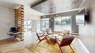 Located at 17444 Slipper Shell Way in Lewes, Delaware, this single-floor community space delivers a sophisticated blend of mid-century modern aesthetics and contemporary design. Throughout, herringbone-patterned hardwood flooring unifies the layout and adds a refined visual rhythm underfoot.

The living lounge area serves as the heart of the space, anchored by a striking textured accent wall in earthy tones and a dramatic tray ceiling with a matching faux-finish treatment. A sculptural multi-bulb chandelier illuminates a curated seating arrangement of wood-framed chairs in white upholstery, centered around a circular coffee table atop a vibrant gold-and-white area rug. Large sliding glass windows flood the room with natural light and offer outdoor views of the surrounding community, including a pool area.

The kitchen is a standout feature, defined by a bold orange ceiling that energizes the space. Sleek, frosted-glass cabinetry, stainless steel counters, a light granite island, and glass pendant lighting combine for a polished, functional aesthetic. Transparent acrylic barstools line the island, creating an inviting bar-style seating area. Geometric mirror wall décor adds an artistic touch.

The dining area is a calm, well-lit room with two rectangular frosted-glass tables, upholstered chairs, and French doors opening to the outdoors, completing this well-appointed gathering space.