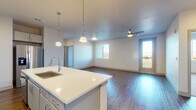This single-floor unit offers a thoughtfully designed open-concept layout with consistent use of wood-look flooring throughout the main living areas. The kitchen serves as a central feature, equipped with grey cabinetry extending to the ceiling, a white quartz island with an undermount sink, subway tile backsplash, stainless steel appliances including a French door refrigerator and electric range, and a dedicated microwave. Three pendant lights hang above the island, providing focused task lighting. The kitchen flows seamlessly into a spacious living area, which is brightened by a large window and a glass door leading to a private balcony with open outdoor views, including distant mountain scenery. A ceiling fan serves the living space.

The bedrooms feature plush carpeting and ceiling fans, with large windows framing expansive mountain and landscape views. The primary bathroom offers a dual-sink vanity with quartz countertops, grey cabinetry, a large mirror, and a separate toilet area, while a secondary bathroom includes a single-sink vanity and a full tub-shower combination. A dedicated utility room houses a full-size washer and dryer alongside the HVAC and water heater systems.