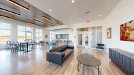Located at 3525 N Peoria Ave in Tulsa, Oklahoma, this single-floor community space offers a thoughtfully designed open-concept layout that seamlessly integrates a living area and a dining room. The interior is anchored by light-toned hardwood-style flooring that runs throughout, complementing the crisp white walls and contributing to a bright, welcoming atmosphere.

The living area features a sleek tufted leather sofa, a round wooden coffee table, and vibrant abstract artwork displayed on the walls, lending the space a contemporary, curated aesthetic. A media console and additional seating add to the room's functionality, while large windows flood the area with natural light.

The dining section is defined by high ceilings accented with warm wood paneling and linear pendant lighting, creating an inviting and distinct atmosphere. Floor-to-ceiling windows along multiple walls offer sweeping outdoor views of the surrounding Tulsa streetscape, bathing the dining tables and mixed seating in generous daylight. A serving counter with a textured dark tile backsplash anchors the rear of the dining area.

Glass-panel double doors with transom windows provide a refined entryway, while a smaller lounge nook with leather accent chairs and a tall window offers a quieter retreat within the space. The overall design balances modern elegance with practical, communal functionality.