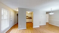 Located at 409 Tradewinds Dr in Fayetteville, NC, this single-floor home offers a practical and comfortable layout with consistent warm-toned hardwood flooring throughout. The open living area is bright and welcoming, featuring neutral gray walls, white baseboards, and natural light streaming in through window blinds. An arched passageway connects the living space to the kitchen, which is equipped with white cabinetry, a coil-top electric range, an overhead exhaust hood, a built-in dishwasher, and rich brown laminate countertops with a stainless steel sink — providing ample storage and workspace. The bedrooms feature the same warm hardwood flooring; one includes a ceiling fan with light fixture and a window overlooking the outdoors, while another offers a spacious, light-filled environment with a large window and clean neutral walls. A closet with a visible rod and shelf provides practical storage. The bathroom includes a full tub-shower combination with built-in wall niches, clean white surround panels, and chrome fixtures. Textured ceilings are present throughout, adding a classic residential character. The floor plan, visible in the dollhouse view, reveals a well-organized, efficiently designed layout suited for everyday living.