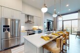 This thoughtfully designed single-floor residence showcases a refined blend of modern and transitional architecture throughout its well-appointed spaces. The gourmet kitchen is a standout feature, boasting white shaker cabinetry extending to the ceiling, a stainless steel appliance suite including a gas range with a professional hood, a French door refrigerator, and a large center island with a crisp white countertop and bar seating. Brushed brass pendant lights suspended from above add warmth to the clean, neutral palette, while rich hardwood flooring ties the space together seamlessly.

The open-concept living area is anchored by soaring ceilings and dramatic floor-to-ceiling windows that flood the room with natural light and frame sweeping outdoor views. A sliding glass door opens directly to a private balcony, further extending the living space. The primary bedroom is a serene retreat, distinguished by a custom sage green paneled accent wall, large windows overlooking the treetop scenery, and plush carpeting underfoot.

The primary bathroom continues the home's refined aesthetic with white cabinetry, a dark stone countertop, an extended vanity with an undermount sink, and a frameless glass-enclosed walk-in shower, delivering a spa-like atmosphere throughout.