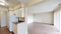 Located at 7 Roger Williams Green in Providence, Rhode Island, this single-floor, two-bedroom, one-bathroom residence offers a practical and comfortable layout across a modest yet well-utilized footprint. Wood-style plank flooring runs consistently throughout, lending a cohesive and clean aesthetic to the entire space.

The living room is generously proportioned, featuring a sliding glass door flanked by vertical blinds that opens to an outdoor view of surrounding greenery, filling the room with natural light. A second window further brightens the space. The open sightline to the kitchen creates a connected, airy feel.

The galley-style kitchen is efficiently designed with white cabinetry, dark granite-style countertops, a gas range, refrigerator, and a double sink. Ample upper and lower cabinet storage lines both walls, providing strong utility in a compact form.

The primary bedroom is comfortably sized, featuring a closet and a window for natural light. The second bedroom also benefits from natural light and dedicated closet space. The full bathroom includes a shower/tub combination with clean white fixtures. A dedicated laundry area houses a full-size washer and dryer, adding significant everyday convenience.
