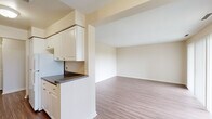 Located at 7 Roger Williams Green in Providence, Rhode Island, this single-floor, two-bedroom, one-bathroom residence offers a practical and comfortable layout across a modest yet well-utilized footprint. Wood-style plank flooring runs consistently throughout, lending a cohesive and clean aesthetic to the entire space.

The living room is generously proportioned, featuring a sliding glass door flanked by vertical blinds that opens to an outdoor view of surrounding greenery, filling the room with natural light. A second window further brightens the space. The open sightline to the kitchen creates a connected, airy feel.

The galley-style kitchen is efficiently designed with white cabinetry, dark granite-style countertops, a gas range, refrigerator, and a double sink. Ample upper and lower cabinet storage lines both walls, providing strong utility in a compact form.

The primary bedroom is comfortably sized, featuring a closet and a window for natural light. The second bedroom also benefits from natural light and dedicated closet space. The full bathroom includes a shower/tub combination with clean white fixtures. A dedicated laundry area houses a full-size washer and dryer, adding significant everyday convenience.