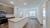 This well-designed two-bedroom, two-bathroom unit offers a thoughtfully arranged single-floor layout that maximizes functionality and comfort. The open-concept kitchen and living area serves as the heart of the space, where a large white quartz island with an integrated sink anchors the kitchen. Flat-front walnut-toned cabinetry extends to the ceiling, providing ample storage, while a full suite of stainless steel appliances — including a side-by-side refrigerator with ice maker, electric range, and built-in microwave — completes the kitchen. The living area receives natural light through wide windows dressed with horizontal blinds and features a ceiling fan overhead. Wood-style plank flooring runs consistently throughout the unit, lending a cohesive, modern aesthetic.

The primary bedroom is generously proportioned, featuring a ceiling fan, a large window, and direct access to a well-appointed en-suite bathroom. The en-suite includes a dual-sink vanity with dark wood cabinetry, backlit mirrors, quartz countertops, and a combination soaking tub and tiled shower. The second bedroom is bright and functional, also equipped with a ceiling fan and a window. Both bedrooms include closets with built-in wire shelving systems. A hallway connects all rooms, and an exterior door provides additional access and natural light to the unit.