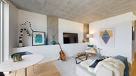 Located at 301 SE 2nd Ave in Portland's vibrant Lower East Side neighborhood, this single-floor unit showcases a thoughtfully designed interior that blends industrial and contemporary aesthetics. The living area is defined by striking exposed concrete ceilings that contrast beautifully with crisp white walls and warm light hardwood flooring, creating an inviting, modern atmosphere throughout.

The open-plan living space offers a well-proportioned layout, with room for comfortable seating arrangements centered around a glass coffee table. The kitchen features sleek, high-gloss navy cabinetry, a textured geometric tile backsplash, stainless steel appliances including an electric range and microwave, and open shelving accented with warm wood tones.

A long hallway connects the living area to the private bedroom, which benefits from natural light and ample storage provided by multiple sliding-door closets. Conveniently positioned in-unit stacked washer and dryer units are tucked neatly along the hallway. The bedroom offers direct access to the bathroom, which is finished with dark stone countertops, a black undermount sink, a warm wood floating shelf, and light tile flooring, lending a refined yet functional feel to the space.