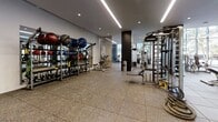 The fitness center at Residences at Bishop Place is a well-appointed, single-level facility designed to support a comprehensive workout experience. The space features a contemporary aesthetic, with a neutral palette of white walls, dark accent columns, and durable rubber-tile flooring throughout. Sleek linear LED lighting runs across the ceiling, complemented by recessed fixtures that provide consistent, bright illumination across the entire floor plan.

The cardio zone is positioned along a dramatic floor-to-ceiling glass curtain wall that frames sweeping views of swaying palm trees and the surrounding cityscape, creating an open, resort-like atmosphere while exercising. A row of Life Fitness treadmills lines this window wall, each equipped with personal display screens.

The strength training area is extensively outfitted with a wide selection of Life Fitness selectorized machines, a multi-functional cable and power rack system, and a full tiered dumbbell rack ranging across multiple weight levels. A dedicated functional training zone houses an organized rack of medicine balls and kettlebells of varying sizes, alongside adjustable benches and battle ropes for dynamic training.

Floor-to-ceiling mirrors are strategically placed to enhance the sense of space and allow for form monitoring. The overall layout is open and uncluttered, offering ample room to move between stations, making this fitness center a thorough and well-designed amenity.