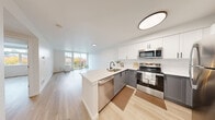 Located at 337 NE 103rd St in Seattle's Northgate neighborhood, this modern 1-bedroom, 1-bathroom unit offers a thoughtfully designed open-concept layout with light hardwood flooring throughout. The combined living, dining, and kitchen area forms the heart of the space, where large floor-to-ceiling windows and a glass-door balcony flood the room with natural light and frame views of the surrounding tree canopy. The balcony provides a comfortable outdoor retreat. The well-appointed kitchen features two-tone cabinetry—white upper cabinets paired with gray lower cabinets—set against a classic subway tile backsplash. A stone-topped peninsula with an undermount sink and a full suite of stainless steel appliances, including a refrigerator, range, and microwave, round out the kitchen. The bedroom is a comfortable, well-lit retreat with a dedicated window overlooking the greenery outside and access to two closets. The clean, minimalist bathroom includes matte black hardware accents against bright white walls and wood-tone flooring. Additional features include an in-unit laundry area, a versatile den, and ample closet storage, making this an efficient and functional urban living space.