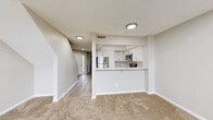 This two-story residence offers a well-organized layout designed for comfortable everyday living. The main level centers around an open-concept living and kitchen area, where the kitchen is defined by a raised bar-style pass-through counter that separates it from the carpeted living space. The kitchen is outfitted with crisp white shaker-style cabinetry, light quartz countertops, and a full suite of stainless steel appliances, including an electric range, over-the-range microwave, and refrigerator. Light wood-style flooring runs through the kitchen and entry hallway, while plush neutral carpet extends throughout the living area and bedrooms. The entry foyer leads naturally into the main living space and provides access to the staircase. Upstairs, the bedrooms are generously proportioned, featuring soft carpet, neutral wall tones, and large windows fitted with horizontal blinds that allow for natural light. One bedroom includes a mirrored sliding-door closet, adding a sense of depth to the room. The bathroom presents a clean, functional design with wood-look vinyl flooring, a white vanity, and a full soaking tub. A textured ceiling throughout the upper level adds subtle architectural character. The overall palette of warm neutrals and white trim creates a bright, cohesive atmosphere across both floors.