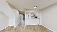 This two-story residence offers a well-organized layout designed for comfortable everyday living. The main level centers around an open-concept living and kitchen area, where the kitchen is defined by a raised bar-style pass-through counter that separates it from the carpeted living space. The kitchen is outfitted with crisp white shaker-style cabinetry, light quartz countertops, and a full suite of stainless steel appliances, including an electric range, over-the-range microwave, and refrigerator. Light wood-style flooring runs through the kitchen and entry hallway, while plush neutral carpet extends throughout the living area and bedrooms. The entry foyer leads naturally into the main living space and provides access to the staircase. Upstairs, the bedrooms are generously proportioned, featuring soft carpet, neutral wall tones, and large windows fitted with horizontal blinds that allow for natural light. One bedroom includes a mirrored sliding-door closet, adding a sense of depth to the room. The bathroom presents a clean, functional design with wood-look vinyl flooring, a white vanity, and a full soaking tub. A textured ceiling throughout the upper level adds subtle architectural character. The overall palette of warm neutrals and white trim creates a bright, cohesive atmosphere across both floors.