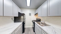 Located at 1293 Bayside Avenue in Woodbridge, VA, this two-bedroom, one-bathroom residence offers a well-organized single-floor layout designed for comfortable everyday living. The living room serves as the heart of the home, featuring soft neutral-toned carpet, a ceiling fan, and a large sliding glass door dressed with vertical blinds that allows generous natural light and outdoor views to fill the space. The galley-style kitchen is thoughtfully appointed with gray shaker cabinetry, marble-look countertops, a white subway tile backsplash, wood-look flooring, and black appliances including a gas range and full-size refrigerator — providing an efficient and stylish cooking environment. Both bedrooms are carpeted and finished in soft gray tones, with the primary bedroom offering a comfortable footprint and natural light from a window with outdoor views. Each bedroom includes closet space with built-in shelving rods, accessible via bifold doors. The full bathroom features a clean, bright aesthetic with a white vanity, round mirror, and a tiled shower-tub combination. The consistent use of light gray walls, white trim, and wood-look flooring in wet areas gives the entire residence a cohesive, move-in ready feel.