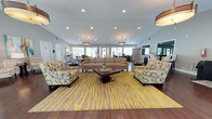 Located at 1660 Old Trolley Rd in Summerville, SC, this single-floor community clubhouse offers a generously scaled, open-concept layout designed for comfort and social gathering. Rich, dark hardwood floors flow throughout the entire space, anchoring a cohesive and polished aesthetic.

The main living area is expansive and inviting, furnished with multiple seating arrangements accented by bold yellow-and-gray patterned chairs and area rugs that add a lively, contemporary flair. Stylish drum pendant light fixtures and recessed lighting provide warm, layered illumination, while vaulted ceilings enhance the sense of openness. A dramatic floor-to-ceiling stacked stone fireplace serves as a focal point, flanked by large windows that flood the room with natural light and offer views of the outdoor surroundings.

A dedicated dining area features a round dark wood table paired with sleek white upholstered chairs, set atop a speckled area rug. Large windows and glass French doors bathe this zone in natural light and provide direct outdoor access.

A built-in service counter with dark cabinetry and granite countertops offers a convenient refreshment station, complete with a coffee setup. The space also includes a high-top bar dining area, adding versatility for both casual and social use. Overall, the space delivers a refined yet welcoming atmosphere ideal for community engagement.