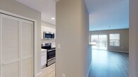 This well-appointed single-floor unit offers a thoughtfully designed open-concept layout that seamlessly connects the kitchen and living area. The kitchen is outfitted with sleek white cabinetry, light quartz countertops, and a full suite of stainless steel appliances including a refrigerator, electric range, over-the-range microwave, and dishwasher. A stacked washer and dryer unit is conveniently located just off the kitchen, adding in-unit laundry functionality. The kitchen flows into a bright, open living area finished with light wood-style flooring and neutral warm-toned walls. Large sliding glass doors open to a private balcony, allowing natural light to fill the living space and providing outdoor views. An additional side window further enhances the brightness of the room. The bedroom is generously sized with the same wood-style flooring, neutral walls, and a closet with bi-fold doors offering practical storage. The bathroom features large-format white tile flooring, a wide vanity with ample counter space and storage, and clean, minimalist finishes throughout. Recessed lighting in the kitchen and consistent flooring choices across the unit contribute to a cohesive, modern aesthetic throughout the space.