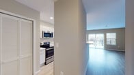 This well-appointed single-floor unit offers a thoughtfully designed open-concept layout that seamlessly connects the kitchen and living area. The kitchen is outfitted with sleek white cabinetry, light quartz countertops, and a full suite of stainless steel appliances including a refrigerator, electric range, over-the-range microwave, and dishwasher. A stacked washer and dryer unit is conveniently located just off the kitchen, adding in-unit laundry functionality. The kitchen flows into a bright, open living area finished with light wood-style flooring and neutral warm-toned walls. Large sliding glass doors open to a private balcony, allowing natural light to fill the living space and providing outdoor views. An additional side window further enhances the brightness of the room. The bedroom is generously sized with the same wood-style flooring, neutral walls, and a closet with bi-fold doors offering practical storage. The bathroom features large-format white tile flooring, a wide vanity with ample counter space and storage, and clean, minimalist finishes throughout. Recessed lighting in the kitchen and consistent flooring choices across the unit contribute to a cohesive, modern aesthetic throughout the space.
