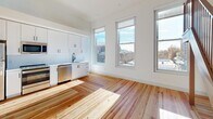 Located at 305 N Second St in Richmond, VA, this thoughtfully designed unit blends classic character with modern finishes throughout its open, single-floor layout. Rich hardwood floors run continuously through every room, lending warmth and cohesion to the entire space.

The entryway welcomes you with clean white walls, built-in storage cabinetry with matte black hardware, and a modern keypad-entry door — setting a functional yet refined tone from the start.

The kitchen is a standout feature, offering a full suite of stainless steel appliances including a gas range, dishwasher, refrigerator, and built-in microwave. Crisp white shaker cabinetry with black hardware lines the walls from floor to ceiling, complemented by white countertops and a stainless steel sink. Tall windows allow natural light to pour in, creating a bright and inviting cooking and dining environment with views of the surrounding Richmond cityscape.

The open living area is expansive and sun-drenched, benefiting from multiple large windows that frame urban views and fill the space with daylight. A handsome wood staircase with a dark metal railing serves as a striking architectural element, anchoring the room and adding vertical drama to the otherwise clean, minimalist aesthetic. Crisp white walls throughout enhance the sense of openness and light.