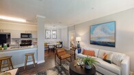 This 2-bedroom, 2-bathroom residence in Baton Rouge, Louisiana offers a thoughtfully designed single-floor layout that balances comfort and functionality. Rich hardwood-style flooring flows continuously throughout the home, anchoring each space with warmth and cohesion.

The open-concept living and dining area forms the heart of the home, where crown molding and neutral walls create a clean, inviting backdrop. The living room offers generous space for seating and entertaining, while the adjacent dining nook provides a cozy setting for meals. A decorative column adds architectural character to the transition between spaces.

The kitchen features granite-look countertops, gray shaker-style cabinetry, and black appliances including a refrigerator, range, microwave, and dishwasher. A breakfast bar with bar stool seating connects the kitchen to the living area, enhancing the open flow. A walk-in pantry or storage closet is accessible directly from the kitchen.

Both bedrooms are comfortably sized and include ceiling fans and windows that allow natural light to fill the rooms. The two bathrooms are well-appointed with granite-top vanities, gray cabinetry, and tub-shower combinations. Crown molding and textured ceilings are consistent throughout the home, lending a finished, polished look to every room.