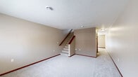 This two-story residence in Sioux Falls, SD offers a well-organized layout spanning two floors of comfortable living space. The main level houses the kitchen, which features warm oak cabinetry, light countertops, tile flooring, and a full suite of appliances including a stainless steel range, built-in microwave, dishwasher, and refrigerator. A pendant light adds a finishing touch, while French doors off the kitchen flood the area with natural light and provide outdoor access. The main floor also includes a spacious carpeted living area with a staircase leading to the upper level. Both bathrooms are finished with tile flooring and warm-toned oak vanities; one includes a full tub-shower combo with chrome fixtures. Upstairs, the two bedrooms are carpeted and feature neutral walls, blinds-covered windows with neighborhood views, and warm oak bi-fold closet doors offering ample storage. The primary bedroom is generously sized with dual closets. A hallway and utility room round out the floor plan. Consistent warm oak woodwork, neutral beige tones, and carpet throughout the upper level create a cohesive and comfortable atmosphere across the entire unit.