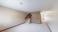 This two-story residence in Sioux Falls, SD offers a well-organized layout spanning two floors of comfortable living space. The main level houses the kitchen, which features warm oak cabinetry, light countertops, tile flooring, and a full suite of appliances including a stainless steel range, built-in microwave, dishwasher, and refrigerator. A pendant light adds a finishing touch, while French doors off the kitchen flood the area with natural light and provide outdoor access. The main floor also includes a spacious carpeted living area with a staircase leading to the upper level. Both bathrooms are finished with tile flooring and warm-toned oak vanities; one includes a full tub-shower combo with chrome fixtures. Upstairs, the two bedrooms are carpeted and feature neutral walls, blinds-covered windows with neighborhood views, and warm oak bi-fold closet doors offering ample storage. The primary bedroom is generously sized with dual closets. A hallway and utility room round out the floor plan. Consistent warm oak woodwork, neutral beige tones, and carpet throughout the upper level create a cohesive and comfortable atmosphere across the entire unit.