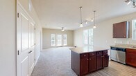 Located in Navarre, FL, this well-appointed 3-bedroom, 2-bathroom residence offers a thoughtfully designed single-floor layout that maximizes comfort and functionality. The open-concept living and kitchen area forms the heart of the home, with plush carpeting throughout the living space and wood-style flooring in the kitchen. The kitchen is outfitted with rich dark-wood cabinetry, granite countertops, stainless steel appliances including a refrigerator, range, microwave, and dishwasher, and a center island with pendant lighting overhead. Track lighting adds a modern touch to the space. The living area is bright and airy, featuring a ceiling fan, multiple windows with blinds, and French doors that open onto a covered balcony with white railings and open views of the surrounding landscape. Each bedroom is carpeted and comfortably sized, with the spacious primary bedroom featuring vaulted ceilings and a dedicated walk-in closet with wire shelving. Both bathrooms mirror each other in design, offering dual-sink vanities with granite countertops, dark cabinetry, wood-style tile flooring, and a tiled tub-shower combination. Two closets provide ample storage throughout the home. The overall aesthetic is clean, neutral, and move-in ready.