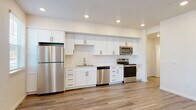 This single-floor residence offers a clean, contemporary design throughout, highlighted by wood-look luxury vinyl plank flooring and a bright, neutral color palette that creates a cohesive and welcoming ambiance.

The kitchen is a standout feature, designed with crisp white shaker-style cabinetry, sleek black hardware, and white countertops. A full suite of stainless steel appliances — including a refrigerator, electric range, microwave, and dishwasher — lines the wall, complemented by recessed lighting above and a single-basin sink. Large windows in the adjacent living area flood the open-concept space with natural light and offer views of the surrounding greenery, further enhancing the airy feel of the main living zone.

The bedrooms are well-proportioned, each featuring the same wood-look flooring and windows that bring in natural light. The bathrooms are finished in a consistent modern style, with white vanities, black hardware accents, white countertops, and large mirrors with stylish vanity lighting. One bathroom includes a full soaking tub with shower, while another offers a more compact layout.

A dedicated laundry closet houses a stacked Whirlpool front-loading washer and dryer alongside a water heater, providing practical, self-contained utility within the residence. The overall design is modern, functional, and move-in ready.
