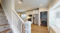 Located at 116 Starlight Walk in Holbrook, NY, this two-story home showcases a clean, modern aesthetic with consistent attention to detail across every room. Warm hardwood-style flooring runs throughout the main and upper levels, complementing soft gray wall tones and crisp white trim work.

The main level centers around an open-concept kitchen and living area. The kitchen is well-equipped with white shaker cabinetry extending to the ceiling, quartz countertops, a peninsula with undermount sink, and a full suite of stainless steel appliances including a gas range, built-in microwave, and French door refrigerator. Pendant lighting adds a refined touch above the peninsula. A dedicated laundry area with a stacked washer and dryer is conveniently positioned nearby. The adjacent living area features crown molding, recessed lighting, a ceiling fan, and a sliding glass door opening to the backyard. A half bath with a marble-accented vanity and mosaic tile flooring completes the main level.

Upstairs, vaulted ceilings lend an airy quality to the bedroom spaces. The primary bedroom includes multiple built-in closets with shelving. A full bathroom features marble-style wall tile, a glass-enclosed tub and shower combination, mosaic basket-weave flooring, and a bright window.