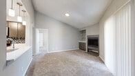 This 1-bedroom, 1-bathroom single-floor residence offers a thoughtfully arranged layout across a comfortable footprint. The living room is a standout space, featuring vaulted ceilings that create an airy, open feel, plush wall-to-wall carpeting, and a tiled fireplace flanked by built-in shelving and cabinetry — an ideal focal point for the room. A large sliding glass door with vertical blinds floods the space with natural light and provides direct access to the outdoors. The entrance opens into the living area and connects seamlessly to the kitchen via a pass-through window, accented by pendant lighting that adds a contemporary touch. The kitchen is equipped with gray cabinetry, white countertops, a mosaic tile backsplash, and stainless steel appliances including an over-the-range microwave. The bedroom is a well-sized retreat with carpet flooring, a ceiling fan, and dual corner windows that invite natural light and outdoor views. It also features direct access to both a dedicated closet and the bathroom. The bathroom is finished with wood-look tile flooring, a white quartz vanity countertop, and a full tub-shower combination clad in large-format gray tile. A separate closet and entrance area complete the unit's functional layout.