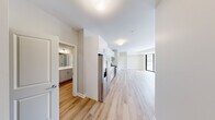 This modern 2-bedroom, 1-bathroom unit at 1200 Broadway Street in Ann Arbor, Michigan offers a well-designed open-concept layout with a clean, contemporary aesthetic throughout. Light wood-tone flooring flows seamlessly across the entire space, complementing the bright, neutral color palette on every wall.

The kitchen is a standout feature, equipped with stainless steel appliances including a gas range, built-in microwave, dishwasher, and a French door refrigerator. White upper cabinetry pairs with light wood-finish lower cabinets, and a white tile backsplash adds a polished touch. Ample counter space and generous cabinet storage make this kitchen both functional and stylish.

The open living area is spacious and sun-drenched, with large floor-to-ceiling sliding glass doors and additional windows that invite abundant natural light and offer views of the surrounding Ann Arbor cityscape. Track lighting adds a modern detail overhead.

Both bedrooms are comfortably sized, each featuring large windows that frame outdoor views and allow natural light to pour in. The primary bedroom offers generous proportions and includes closet storage.

The bathroom is finished with a wide vanity featuring white quartz countertops, grey cabinetry with brushed nickel hardware, and a large wall mirror. Two closets provide additional storage throughout the unit.