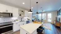Located at 1223 E Plant St in Winter Garden, FL, this model 1-bedroom, 1-bathroom unit showcases a thoughtfully designed single-floor open-concept layout with contemporary finishes throughout. The kitchen is a standout feature, outfitted with white shaker cabinetry, matte black hardware, a striking marble-look tile backsplash, quartz countertops, and stainless steel appliances including a French door refrigerator, range, microwave, and dishwasher. A central island with seating provides both additional prep space and casual dining. Pendant lighting and recessed fixtures illuminate the space, while open shelving adds a decorative, functional touch. The kitchen flows seamlessly into the living area, which is bathed in natural light from multiple windows and a glass door that opens to a private balcony with outdoor views. Wood-look flooring extends throughout the main living areas, adding warmth and continuity. The bedroom offers a comfortable, well-proportioned retreat. The bathroom features clean white subway tile surrounding a soaking tub, maintaining the home's crisp, modern aesthetic. Ceiling fans in the living area contribute to comfort and airflow. The overall ambiance is bright, clean, and welcoming, reflecting a well-appointed modern design ideal for everyday living.