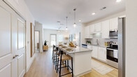 Located at 12020 Brush Hill Rd in Wildwood, Florida, this thoughtfully designed 2-bedroom, 2-bathroom residence offers a bright, modern living experience on a single floor. The open-concept layout connects the kitchen, dining, and living areas seamlessly, creating an inviting and functional space. The kitchen is a standout feature, showcasing white shaker cabinetry, granite countertops, stainless steel appliances, and a central island with pendant lighting and bar seating — ideal for casual dining and entertaining. Light wood-style flooring flows throughout the main living areas, enhancing the airy, contemporary aesthetic. The living room receives abundant natural light through large windows and a glass door, adding warmth and openness to the space. Both bathrooms are finished with granite vanity countertops, white cabinetry, and wood-look flooring. One bathroom features a walk-in shower, while the other includes a tub-shower combination. The spacious primary bedroom offers a ceiling fan, direct bathroom access, and a generously sized walk-in closet with wire shelving. The second bedroom is equally well-lit, with large windows and a ceiling fan. Throughout, the residence maintains a clean, neutral palette with modern finishes that convey a sense of comfort and quality.